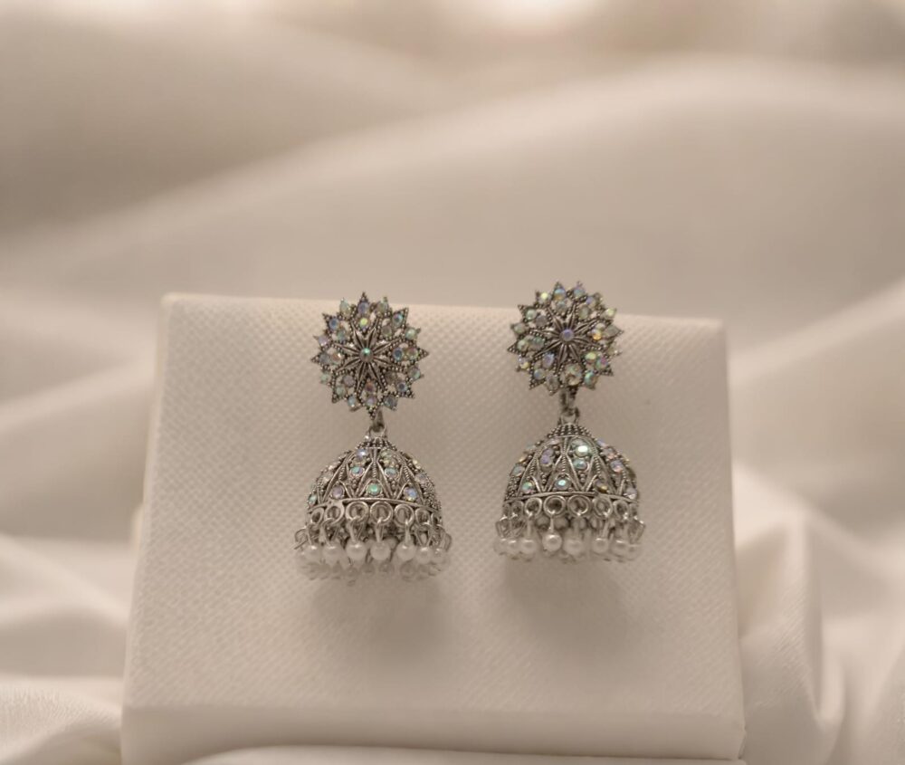 Elegant silver jhumka earrings with intricate floral tops, shimmering stones, and delicate pearl danglings.