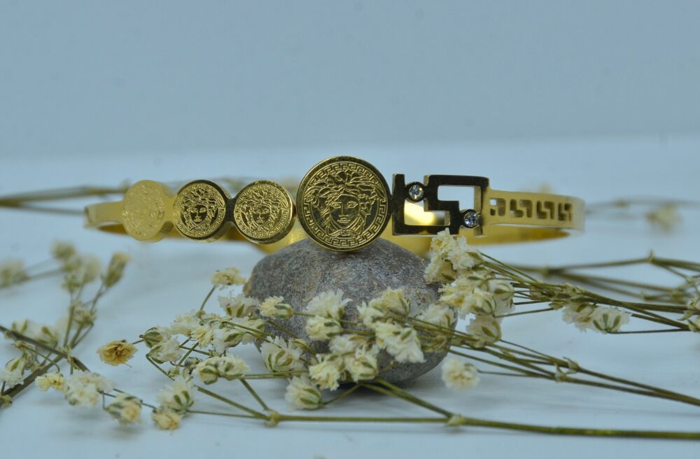 Gold-plated bracelet adorned with engraved Medusa-style coin motifs and a geometric clasp accented