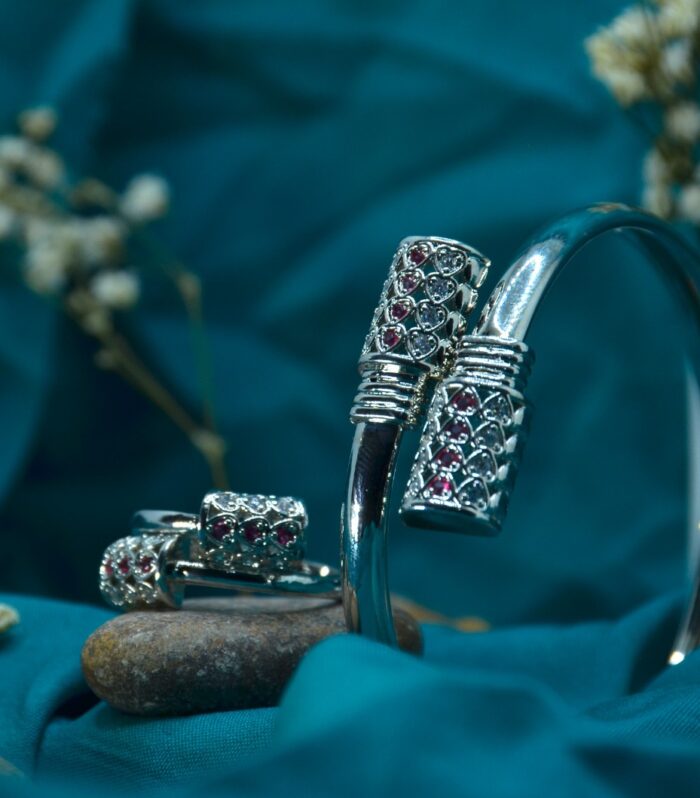Elegant silver jewelry set featuring a bracelet and matching rings adorned with red and white gemstones in a lattice design.