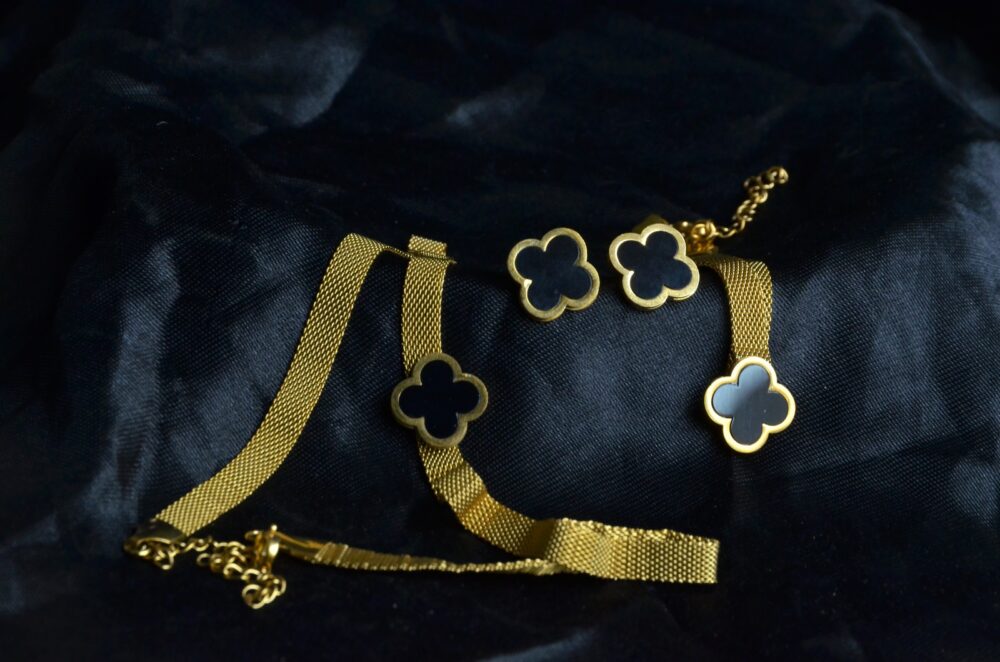 Chic gold jewelry set featuring a clover motif with black enamel accents on a textured chain.