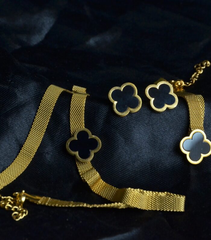 Chic gold jewelry set featuring a clover motif with black enamel accents on a textured chain.