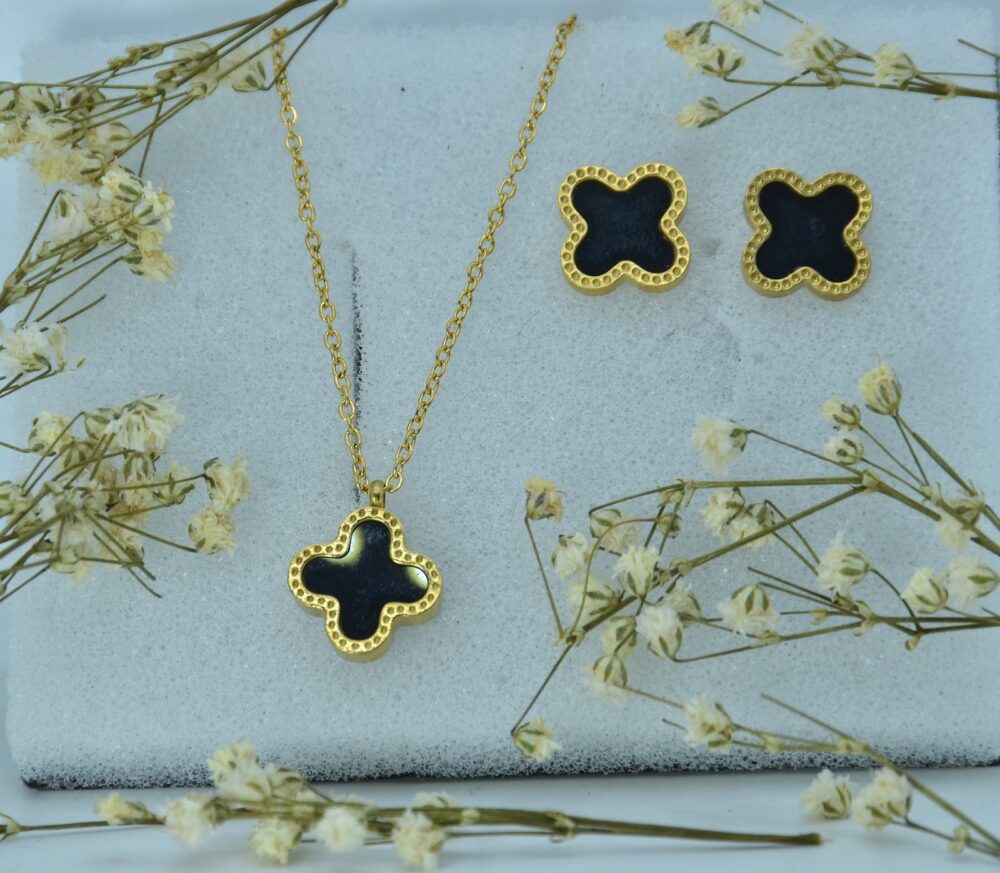 Elegant gold jewelry set featuring a black clover-shaped pendant and matching stud earrings with textured borders.