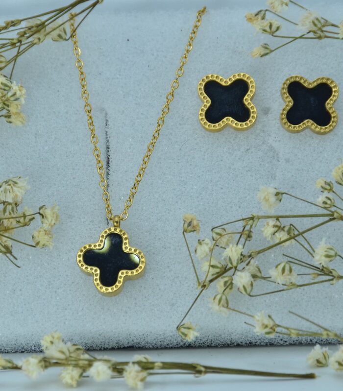 Elegant gold jewelry set featuring a black clover-shaped pendant and matching stud earrings with textured borders.
