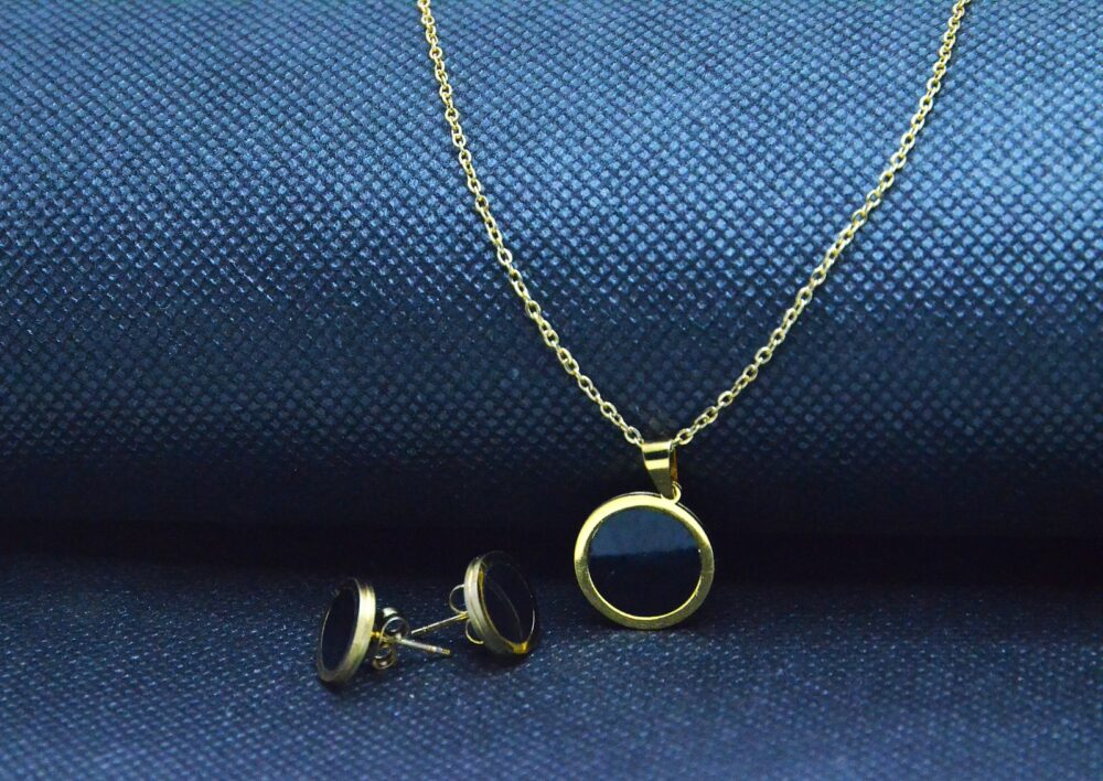 Elegant gold jewelry set with a round black enamel pendant and matching stud earrings